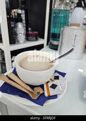 Eine weiße Kaffeetasse mit einem Löffel darin steht auf einem blauen Serviette auf einem Tisch. Die Tasse ist mit Kaffee gefüllt und es liegen zwei Zuckerpäckchen auf der Serviette. T Stockfoto