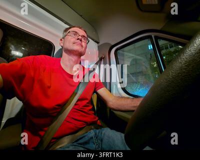 Mann in einem roten Hemd fährt einen LKW. Er trägt eine Brille und hat den Sicherheitsgurt angelegt Stockfoto