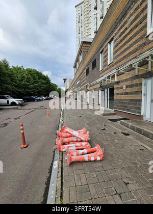 Reihe von Orangenkegeln oder Straßensäulen stehen auf dem Gehweg vor einem Gebäude. Es stehen auch mehrere Autos auf der Straße in der Nähe des Eingangs in der c Stockfoto