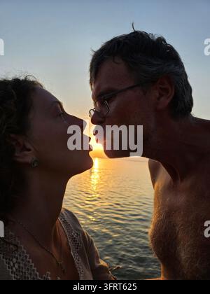 Mann und Frau küssen sich im Ozean. Der Mann trägt eine Brille Stockfoto