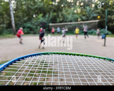 Ein Tennis-Badminton-Schläger wird mit einer Nahaufnahme des Netzes gezeigt. Das Bild zeigt eine Gruppe von Menschen, die auf einem Feld Volleyball spielen Stockfoto