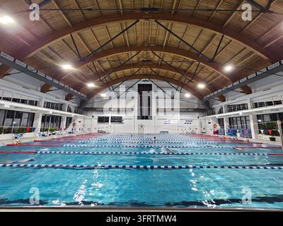 Moskau - 09. Oktober 2025: Großes Hallenbad mit klarem blauem Wasser. Reihen von Bahnen, die mit schwimmenden Trennwänden markiert sind. Hohe gewölbte Decke mit freiliegenden Holzbalken. Lichter beleuchten den Raum Stockfoto
