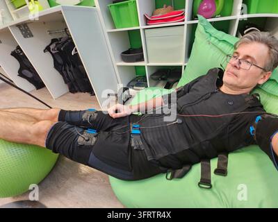 Mann ruht auf grünem Sitzsack. Trägt schwarze Sportkleidung und Brille. Liegt in entspannter Pose auf einer lebhaften grünen Oberfläche. Der Hintergrund zeigt Regale mit Stockfoto