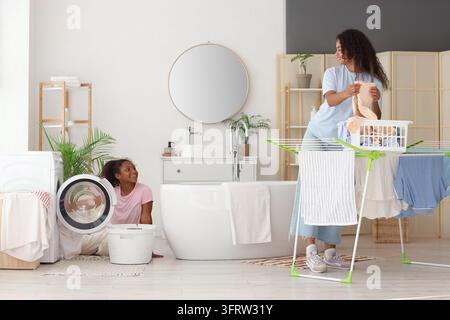 Familienpflichten und Haushaltsverantwortung, Mutter und Tochter waschen gemeinsam Wäsche in einem hellen modernen Badezimmer mit Wäsche, die auf einem Wäscheständer trocknet Stockfoto