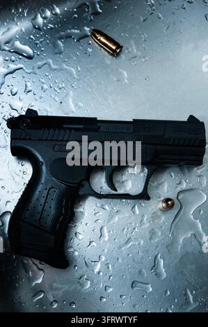 Eine schwarze Walther P22-Pistole mit der Markierung 6 mm BB ruht auf nassem Metall neben zwei messingfarbenen kugelförmigen Gegenständen Stockfoto