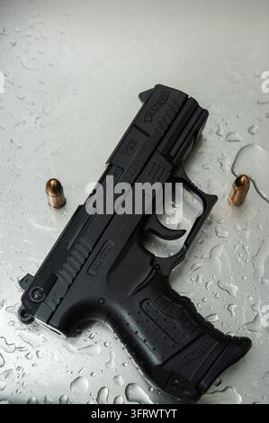 Eine schwarze Walther P22-Pistole mit der Markierung 6 mm BB ruht auf nassem Metall neben zwei messingfarbenen kugelförmigen Gegenständen Stockfoto
