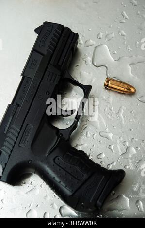 Eine schwarze Walther P22-Pistole mit der Markierung 6 mm BB ruht auf nassem Metall neben zwei messingfarbenen kugelförmigen Gegenständen Stockfoto