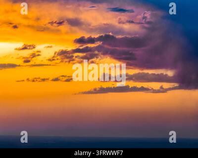 Warmes, glühendes orangefarbenes und gelbes Abendlicht, das hinter violetten Gewitterwolken strahlt Stockfoto