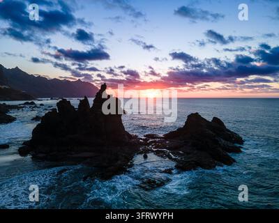 Klippen ragen in voller Silhouette vor einem lebhaften rosafarbenen und orangefarbenen Sonnenuntergang über der Anaga-Küste. Der dramatischste Abschluss der Luftaufnahmen des Tages Stockfoto