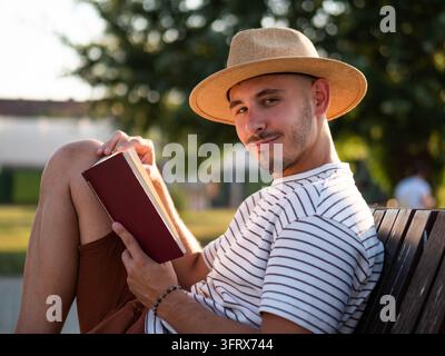 Nachdenklicher erwachsener Mann entspannt sich im Park, er liest ein Buch. Stockfoto