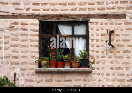 Ein hölzernes Fenster in der Mitte einer Wand aus Stein und Ziegelstein. Vor dem Fenster stehen Topfpflanzen. Stockfoto
