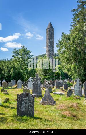 Ansicht von Grabsteinen und dem runden Turm in den Ruinen des Klosterdorfs Glendalough, County Wicklow, Irland Stockfoto