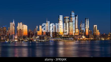 Abendansicht von New York City mit der Skyline von Midtown Manhattan von der anderen Seite des Hudson River aus, wobei die Wolkenkratzer von Hudson Yards im Abendlicht leuchten. USA Stockfoto