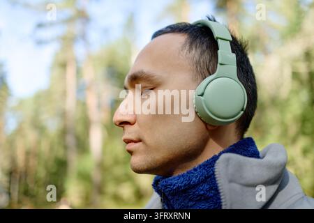Mann mit Kopfhörern hört Musik im Wald Stockfoto