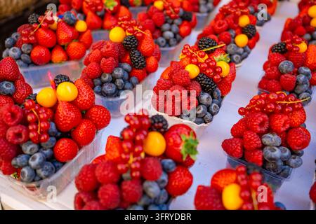 Verschiedene frische Beeren in klaren Behältern angeordnet mit Erdbeeren, Himbeeren, Blaubeeren, Brombeeren und Kirschen an einer Marktauslage Stockfoto