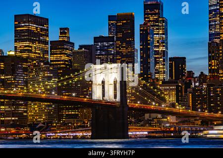New York, USA - 25. September 2026: Beleuchtete Brooklyn Bridge und Wolkenkratzer des Finanzdistrikts bei Nacht über dem East River Stockfoto