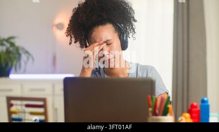 Gestresste Frau unterrichtet online mit einem Laptop und Headset zu Hause Stockfoto