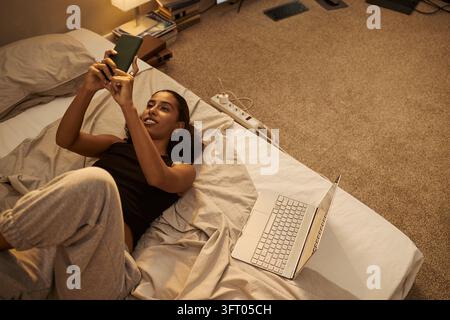 Bikolorige Frau verwendet Smartphone, während sie im Bett entspannt Stockfoto