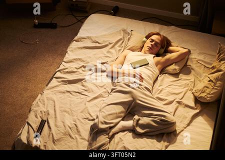 Mann schläft auf Matratze, während er Musik mit Kopfhörern hört Stockfoto