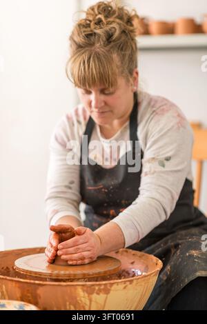Künstlerin arbeitet mit feuchtem Ton auf einer Töpferscheibe, formt das Material mit ihren Händen, erschafft handgefertigte Keramik in einem hellen Atelier, umarmt c Stockfoto