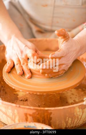 Geschickte Handwerkerhände formen sorgfältig feuchten Ton auf einer sich drehenden Töpferscheibe und stellen ein Keramikgefäß her, um den kreativen Prozess des Töpferhandwerks zu demonstrieren Stockfoto