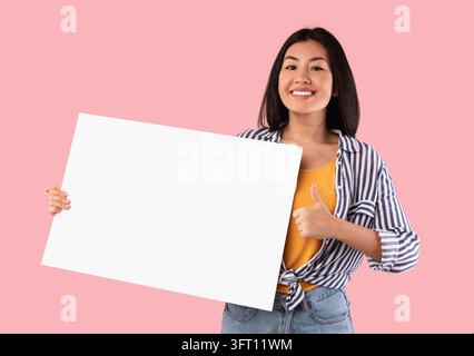Porträt Einer Fröhlichen Asiatischen Frau, Die Daumen Hoch Zeigt Zeichen Geste Und Leeres Papier Poster Für Ihren Text Hält Stehend Mit Weißem Quadratischem Brett Für Adve Stockfoto
