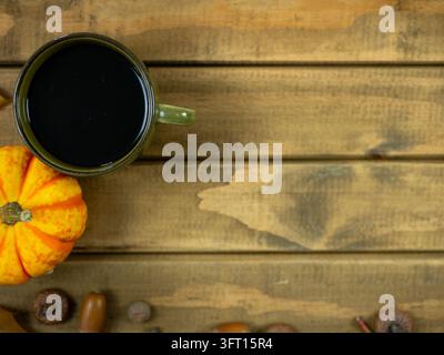 Minimale Herbst-Kaffeeszene mit dunkler Tasse und orangefarbenem Kürbis auf hellem Holztisch, Oktober-Getränkehintergrund mit Kopierraum Stockfoto