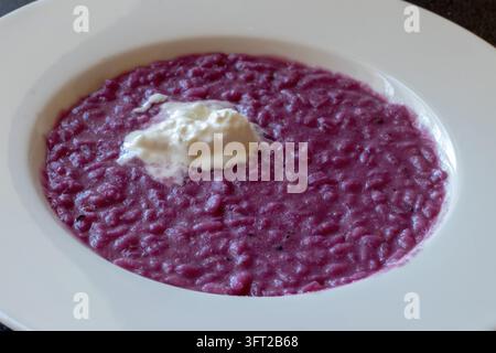 Hochwinkliger Nahaufnahme von magenta-farbigem Kohlsalat-Risotto mit einem Löffel Stracciatella-Käse in einer weißen Schüssel, mit cremiger Stracciatella oben drauf Stockfoto
