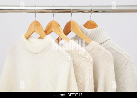 Garderobenständer mit Kleiderbügeln und Pullovern auf hellem Hintergrund Stockfoto