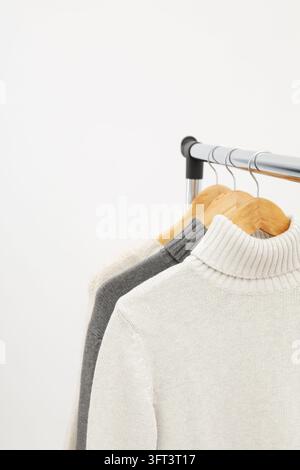 Garderobenständer mit Kleiderbügeln und Pullovern auf hellem Hintergrund Stockfoto