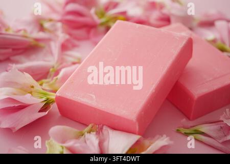 Zwei rosa Seifenstücke, umgeben von rosa Blütenblättern auf einer Oberfläche Stockfoto
