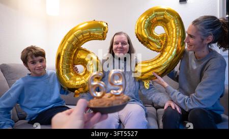 Familienmitglieder feiern einen Geburtstag mit Ballons und Geburtstagstorte mit Kerzen Stockfoto
