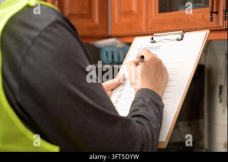 Malerbeiter inspiziert Holz-Küchenregal und hält Papiercheckliste für die Wohnsicherheitsüberprüfung. Stockfoto