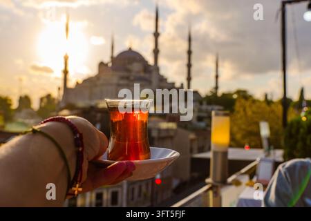 Hand, die ein Glas türkischen Tee hält, mit einer Moschee im Hintergrund in Istanbul Stockfoto