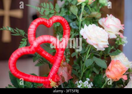 Zwei rote Herz-Dekorationen auf frischem Rosenstrauß in einer Kircheneinrichtung Stockfoto