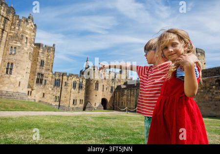 Zwei Kinder genießen einen sonnigen Sommertag auf einer historischen Burg, eines zeigt auf die Struktur, während das andere lächelt und ihre Freude zeigt Stockfoto
