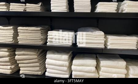 Ordentlich gefaltete Badetücher in Grau, Beige und Weiß, gestapelt auf schwarzen Regalen in einem Heimtextilgeschäft Stockfoto
