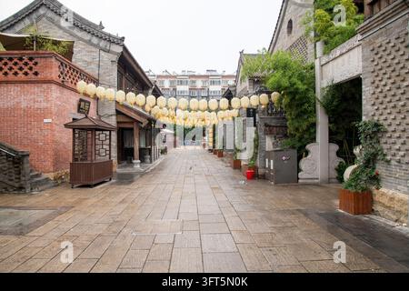 Gelbe Laternen, die über eine ruhige gepflasterte Gasse zwischen traditionell gestalteten Backsteingebäuden in Luoyang, Henan, China, gespannt sind. Stockfoto