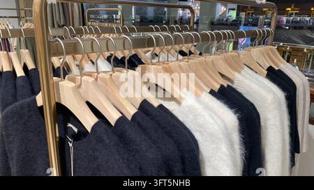 Weiche, flauschige Strickpullover in Schwarz, Weiß und Beige, die an Holzbügeln in einem Modeeinzelhandelsgeschäft hängen Stockfoto