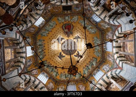 INTRIKATE GOLDENE MOSAIKKUPPEL UND KRONLEUCHTER, AACHENER DOM, AACHEN, DEUTSCHLAND: Ein direkter Blick nach oben auf das atemberaubend detaillierte goldene Mosaik an der achteckigen Kuppeldecke einer historischen Kapelle, mit einem massiven, kunstvollen Kronleuchter, der zentral hängt. INFO: Der Aachener Dom, Deutschlands erstes UNESCO-Weltkulturerbe, ist ein karolingisches Architekturmeisterwerk, das von Karl dem Großen gegründet wurde. Diese historische Stätte, die byzantinische und gotische Elemente vereint, diente als Krönungskirche für einunddreißig deutsche Monarchen. Stockfoto