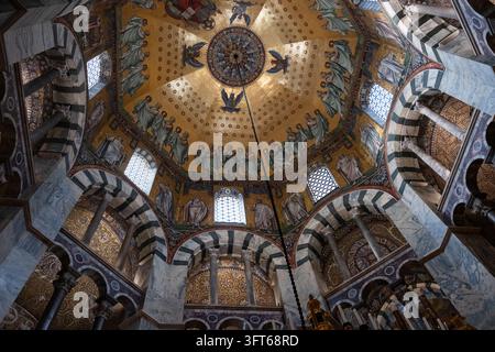 INTRIKATER GOLDENES MOSAIKKUPPEL, AACHENER DOM, AACHEN, DEUTSCHLAND: Ein direkter Blick nach oben auf das atemberaubend detaillierte goldene Mosaik an der oktogonalen Kuppeldecke der historischen alten Kathedrale. INFO: Der Aachener Dom, Deutschlands erstes UNESCO-Weltkulturerbe, ist ein karolingisches architektonisches Meisterwerk, das von Karl dem Großen gegründet wurde. Diese historische Sehenswürdigkeit, die byzantinische und gotische Elemente vereint, diente als Krönungskirche für einunddreißig deutsche Monarchen. Stockfoto