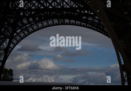 Verzierte Eisenbogenbasis des Eiffelturms, die einen bewölkten Himmel in Paris, Frankreich, einrahmt. Stockfoto
