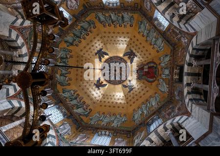 INTRIKATE GOLDENE MOSAIKKUPPEL UND KRONLEUCHTER, AACHENER DOM, AACHEN, DEUTSCHLAND: Ein direkter Blick nach oben auf das atemberaubend detaillierte goldene Mosaik an der achteckigen Kuppeldecke einer historischen Kapelle, mit einem massiven, kunstvollen Kronleuchter, der zentral hängt. INFO: Der Aachener Dom, Deutschlands erstes UNESCO-Weltkulturerbe, ist ein karolingisches Architekturmeisterwerk, das von Karl dem Großen gegründet wurde. Diese historische Stätte, die byzantinische und gotische Elemente vereint, diente als Krönungskirche für einunddreißig deutsche Monarchen. Stockfoto