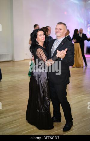 Eine Frau in einem langen schwarzen Kleid mit durchsichtigen gepunkteten Ärmeln tanzt mit einem Mann in einem dunklen Anzug auf einem Ball. Stockfoto
