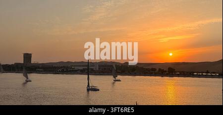 Beobachtung des Sonnenuntergangs auf dem Nil in Assuan in Ägypten. Mehrere Segelboote kreuzen den Fluss und befördern Touristen und Einheimische Stockfoto