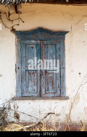 Detaillierte vertikale Aufnahme von verwitterten blauen Holzläden an einer alten rustikalen weiß getünchten Lehmwand Stockfoto