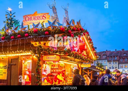 Bamberg, Deutschland – 28. November 2025. Touristen kaufen süße Churros an einem beleuchteten Stand des Bamberg-Weihnachtsmarktes. Stockfoto
