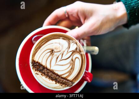 Luftbild einer roten Kaffeetasse mit beeindruckender Rosette aus Latte Art, die die Fähigkeiten des Barista und die Handwerkskunst des Kaffees hervorhebt. Stockfoto