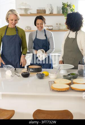 Drei Freundinnen tragen Schürzen und bereiten in der heimischen Küche einen Schichttorte mit Springformpfanne vor Stockfoto