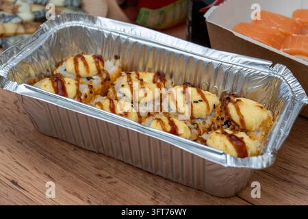 Gebackene Sushi-Rollen mit Sauce in einer Folienlieferbox Stockfoto